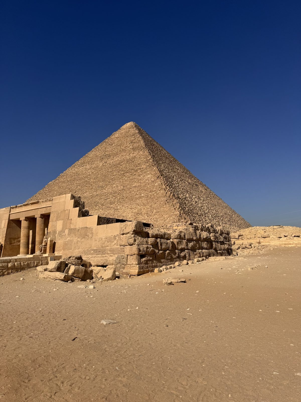 Ruins of a small temple with columns, pyramid visible behind