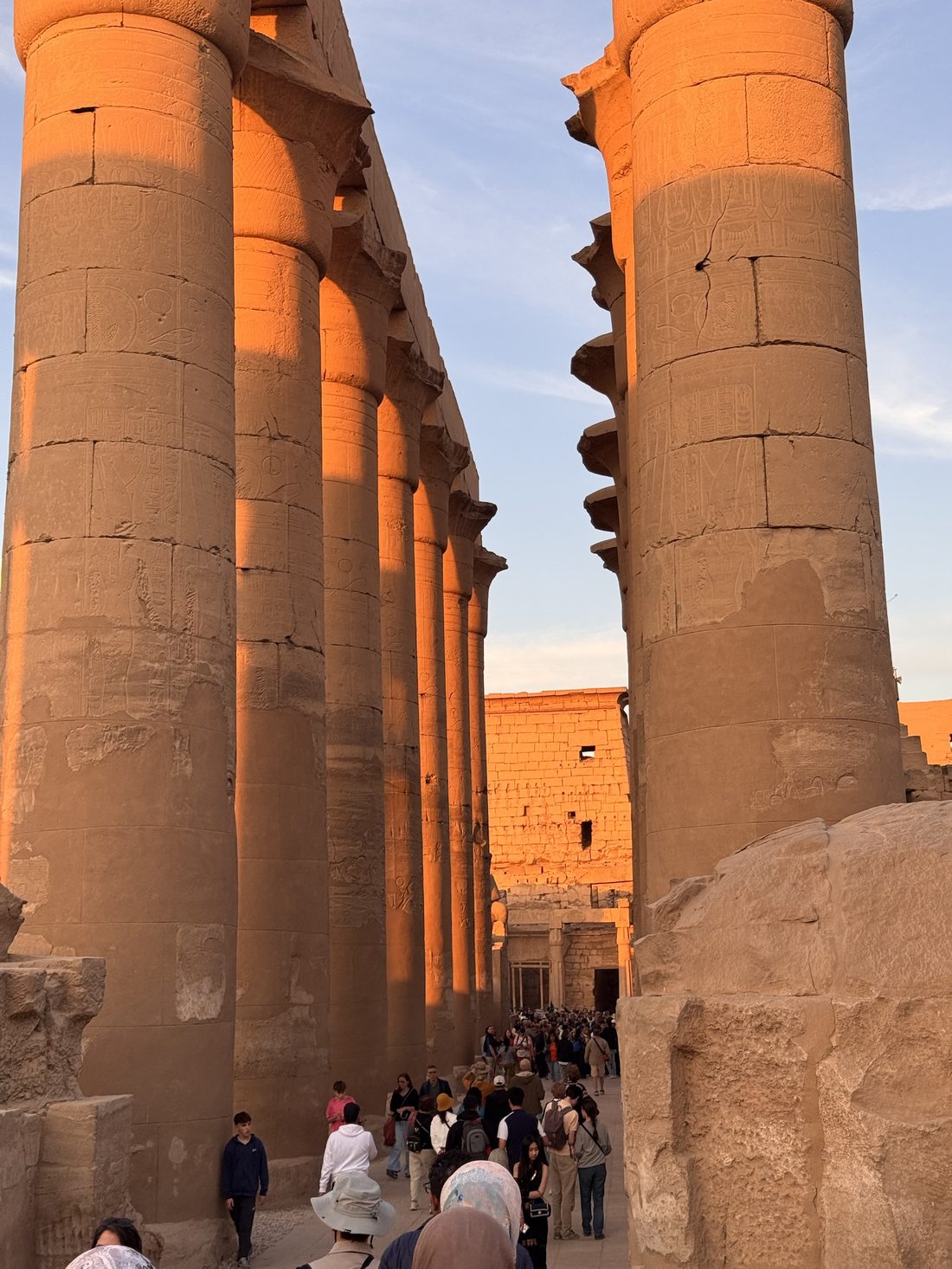 Visitors walking through the colonnade of Luxor Temple at golden hour