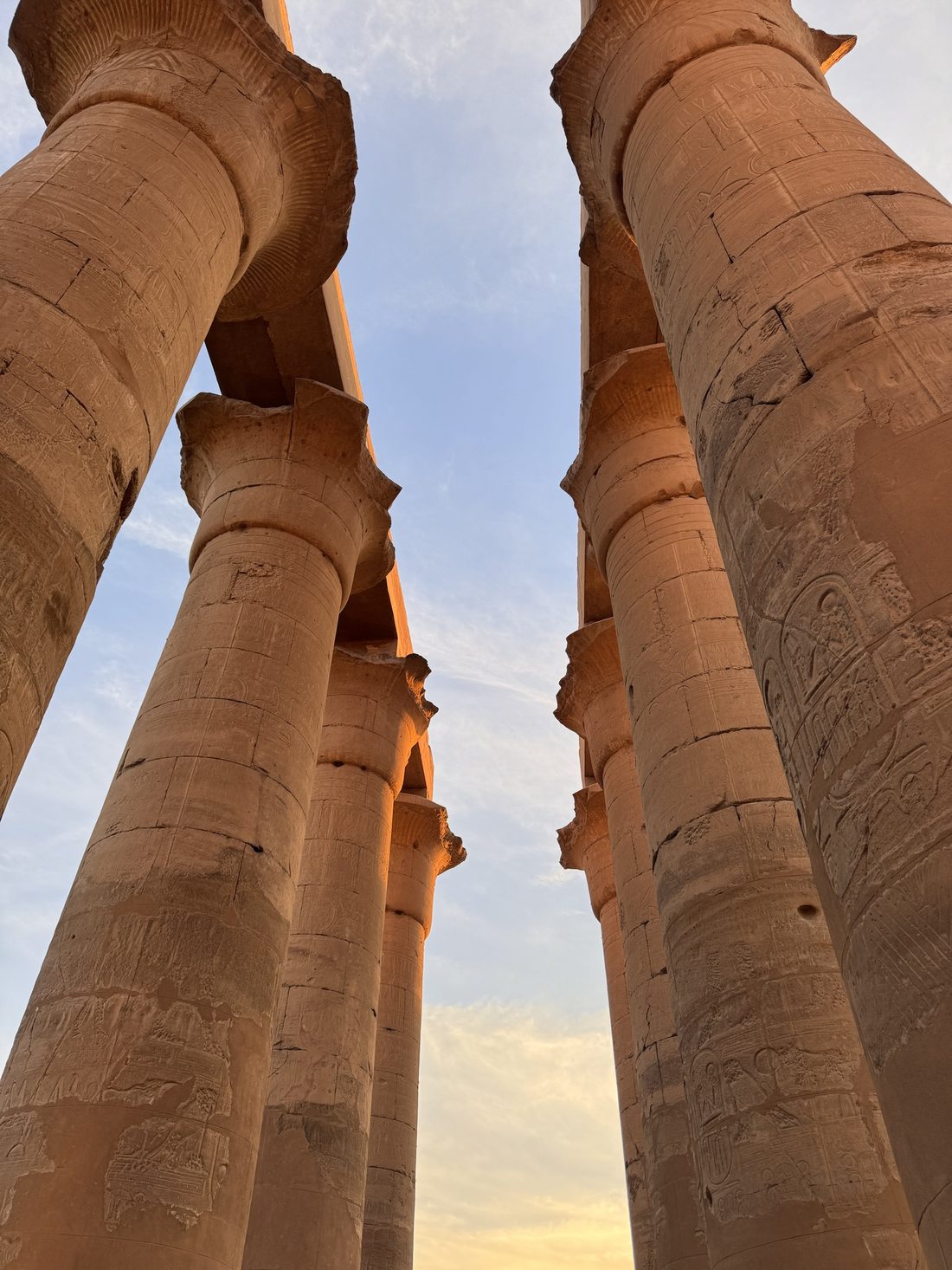 Looking up at the carved papyrus columns of Luxor Temple against the sky